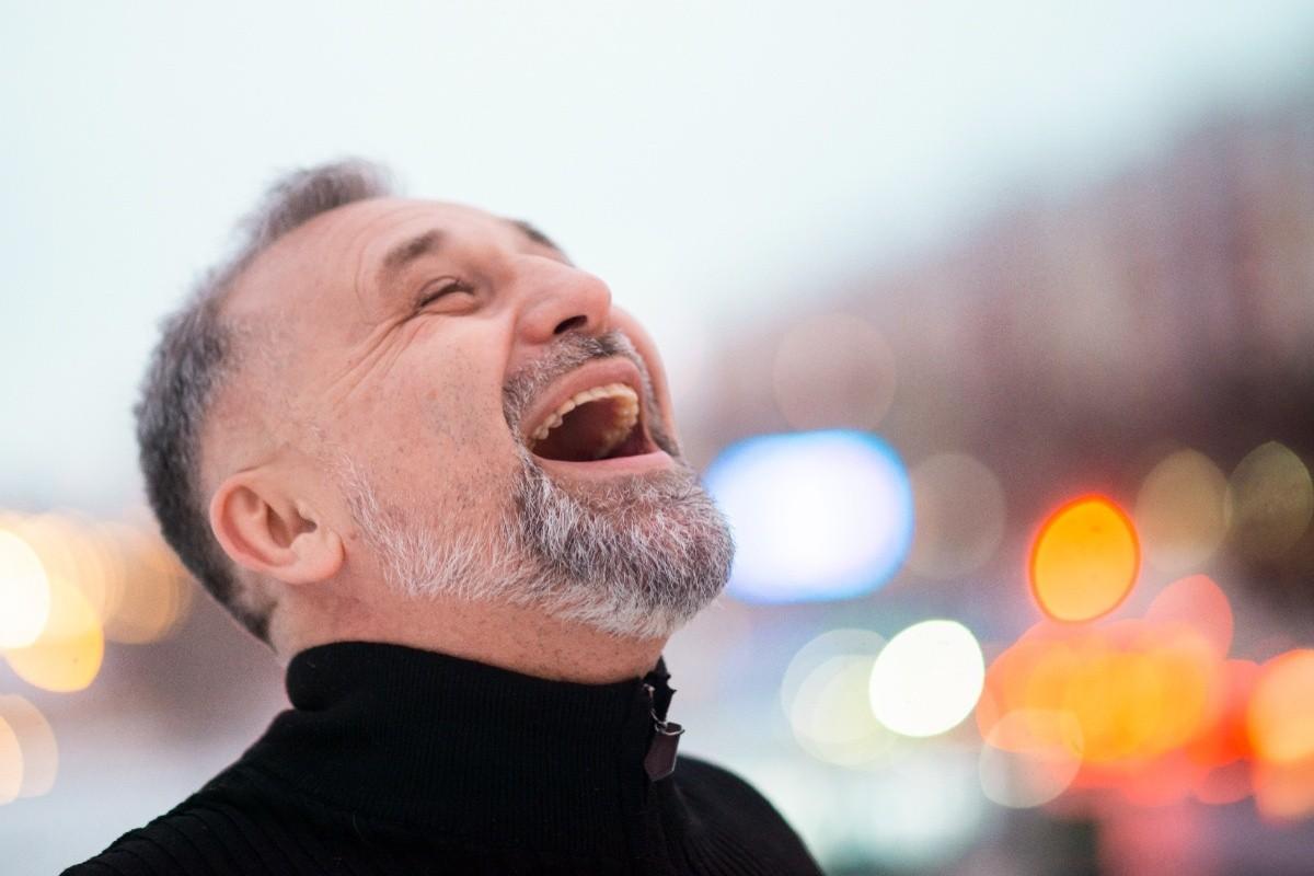 Older man smiling confidently outdoors, showing missing teeth while laughing in a city