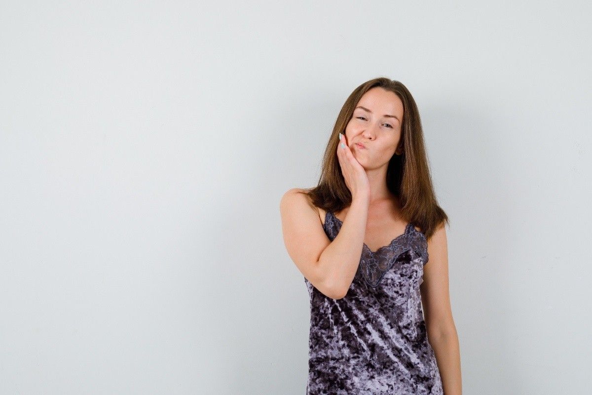 Woman holding her cheek with tooth pain against a gray background